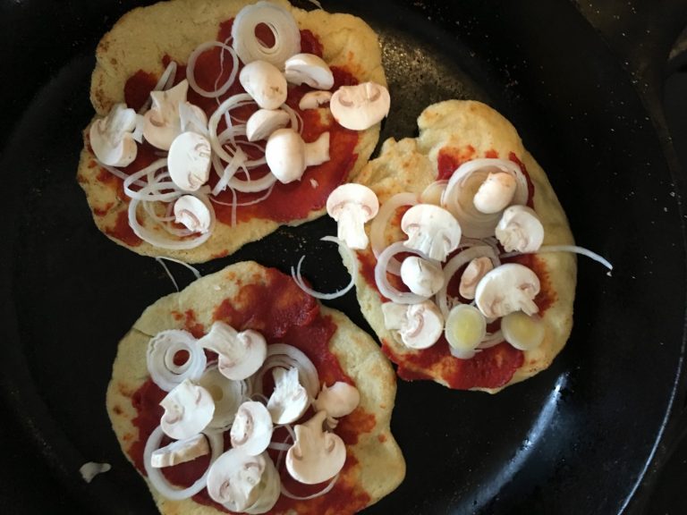pan pizzas with tomato, onion and mushrooms in a cast iron pan from above