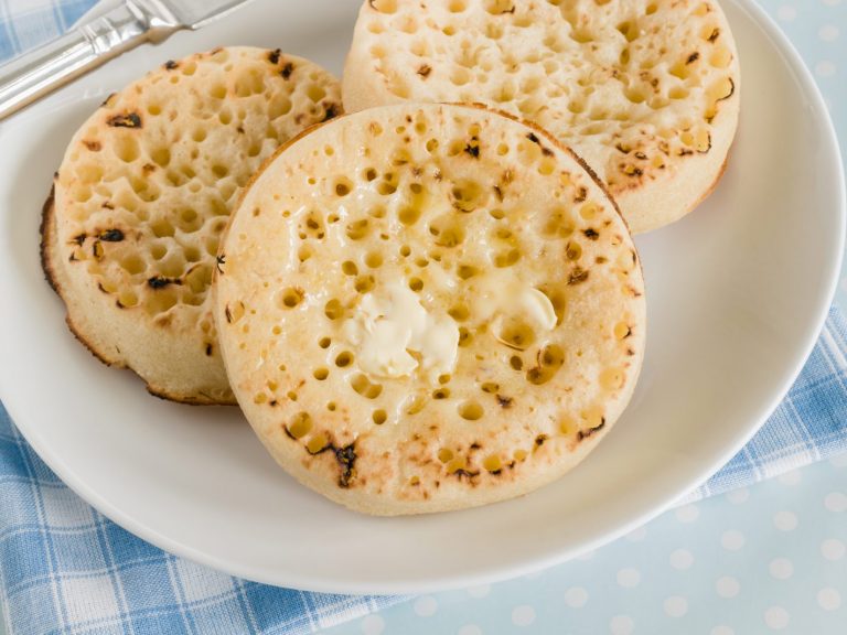 buttered crumpets on a white plate with a blue and white checkered napkin