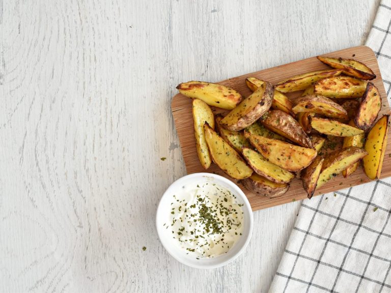 potato wedges on a white background with a cream mayonnaise dip. a cooling tray is in the corner