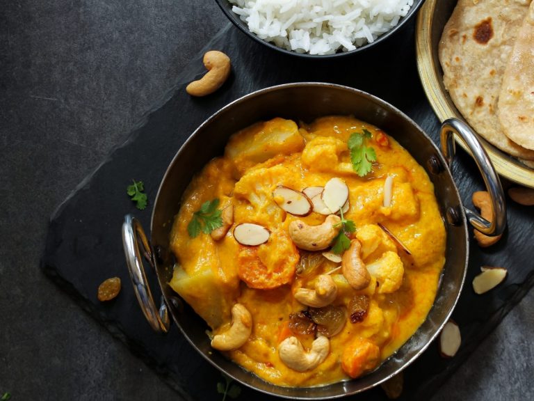 chicken curry in a pan with rice and cashews on a black backgound