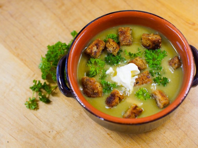Pea and ham soup in a brown bowl with croutons, creme fraiche and parsley